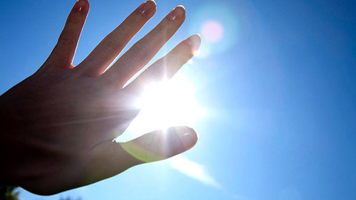 Close-up of hand in front of blue sky with burning sun --- Image by ?beyond/Corbis